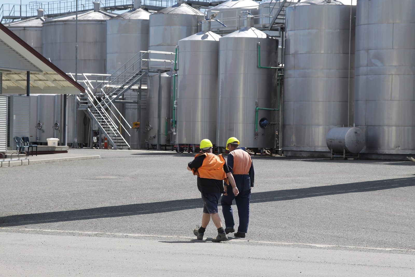 Workers walking past large stainless-steel wine tanks