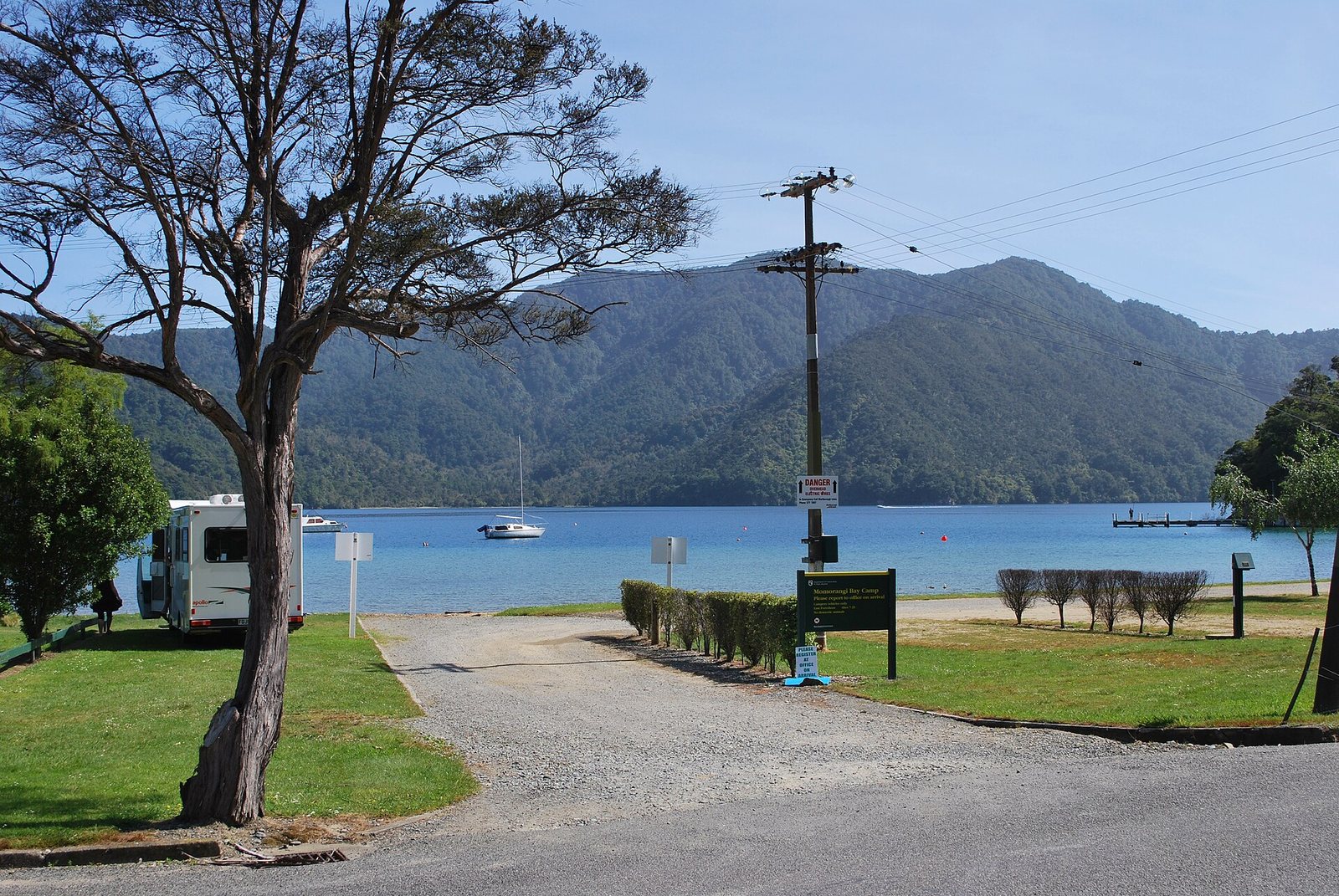 Tents and vans on grass beside the water at Momorangi Bay campsite