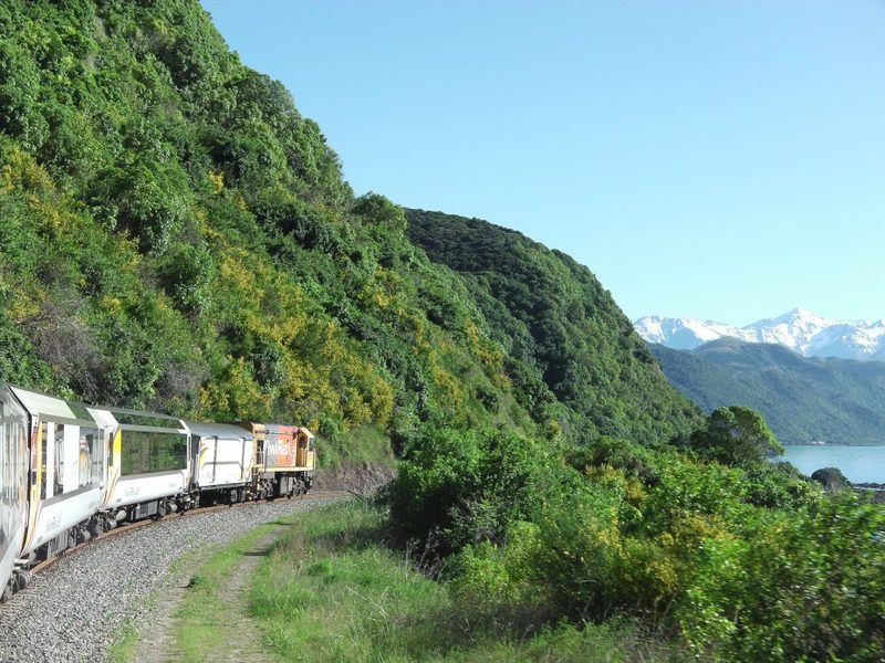 Coastal Pacific passenger train rounding the Kaikōura coastline beside the sea and mountain ranges.