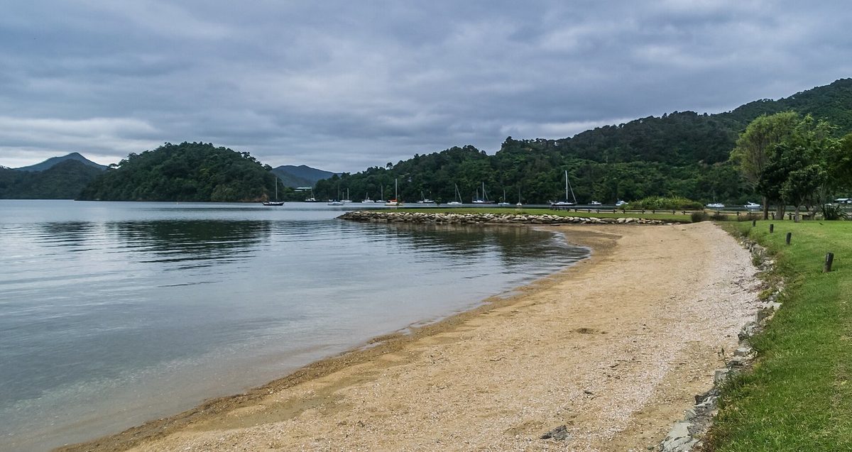 Ngakuta Bay's curved beach, calm water, moored yachts and bush-clad shoreline.