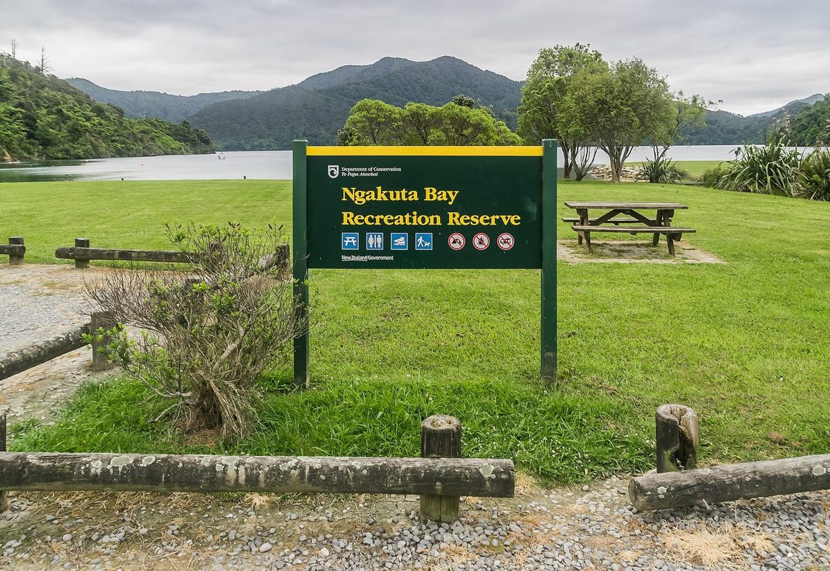 Ngakuta Bay Recreation Reserve sign, picnic lawn and the sheltered bay beyond.