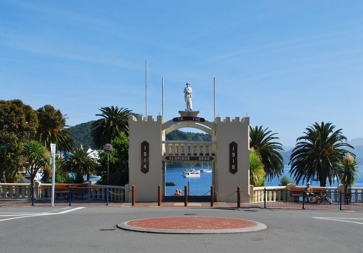 Picton's war memorial arch on London Quay, framed by palms with the harbour visible through it.