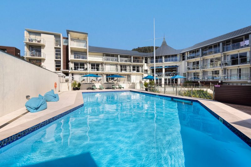Outdoor swimming pool and surrounding Edit Picton hotel buildings under a clear blue sky.