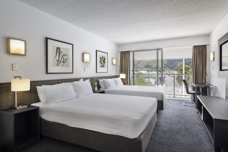 Bright guest room with two beds, a work desk, balcony doors and a view toward Picton's hills.