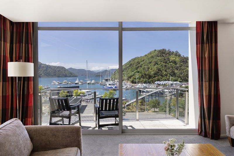 Harbour and Marlborough Sounds view through the picture window and balcony of an apartment lounge.