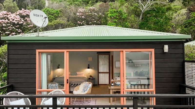 Front of Seascape Cottage with open glazing, private deck seating and native bush behind.