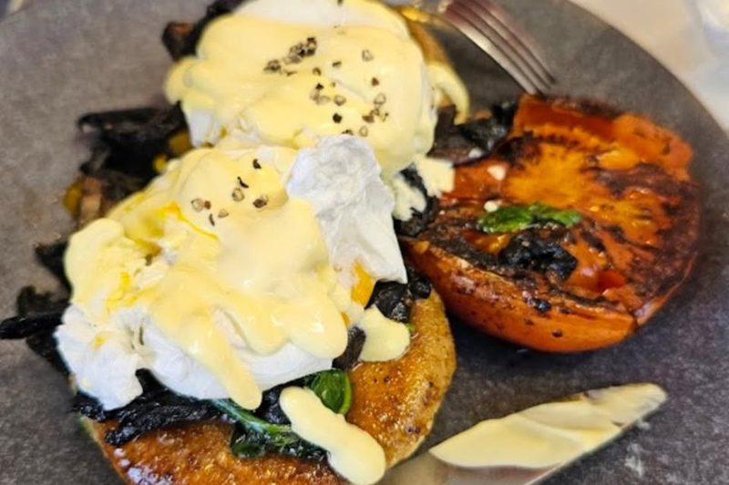 Eggs Benedict with mushrooms and grilled tomato on a cafe plate.