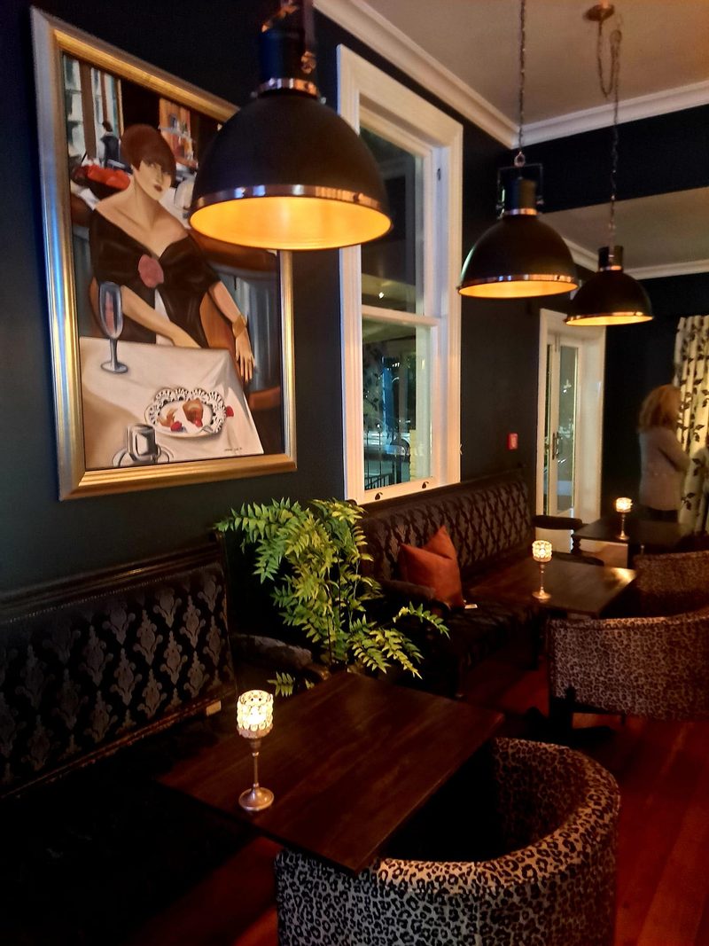 Wine bar seating with dark walls, pendant lights, patterned chairs, banquettes and candlelit tables.