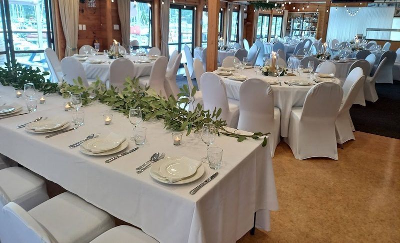 The Wardroom arranged with round dining tables, white chairs and marina views through the windows.