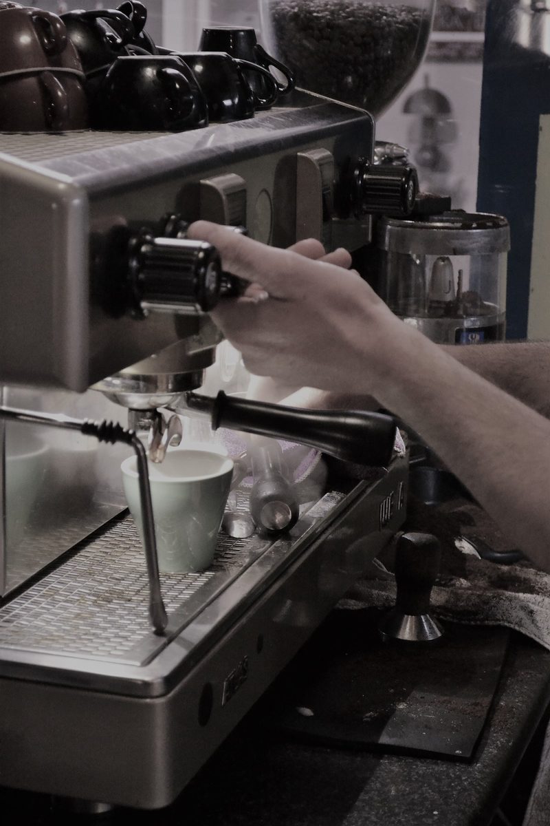 Barista operating the cafe's espresso machine, with cups and coffee grinder visible.
