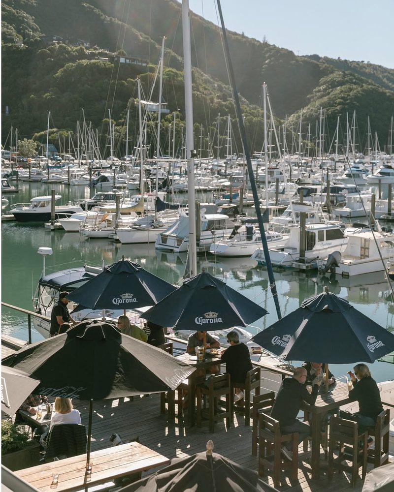 Outdoor dining deck with tables and umbrellas overlooking the densely moored Waikawa Marina.