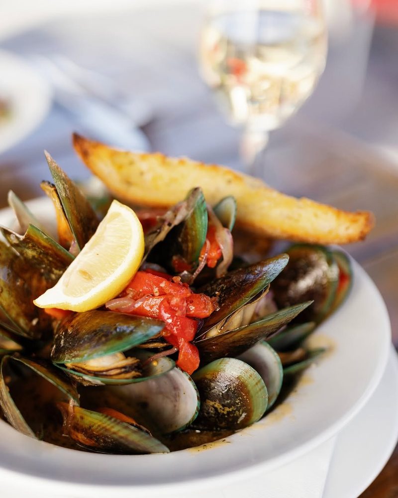 Bowl of green-lipped mussels in tomato broth with lemon and toasted bread.