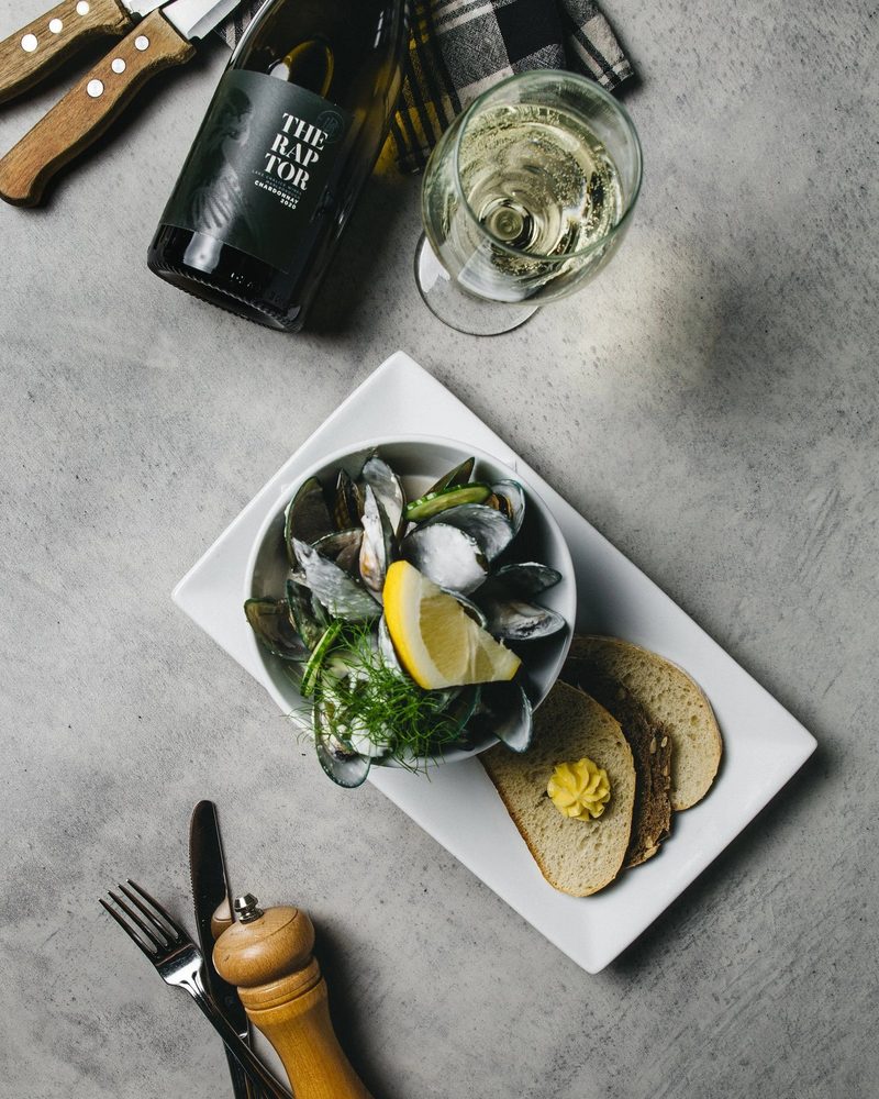 Bowl of green-lipped mussels with bread, lemon and a glass and bottle of Marlborough chardonnay.
