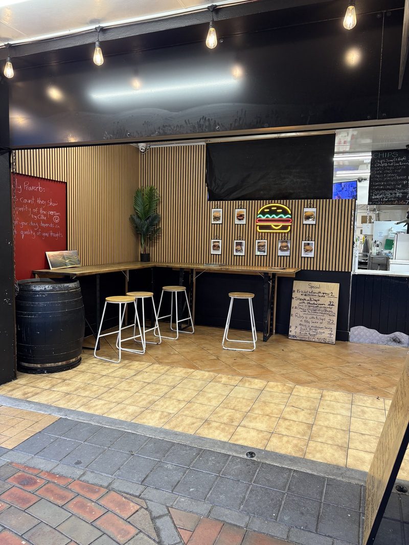 Sheltered customer ledge and stools beneath Paperfish's burger display and neon burger sign.