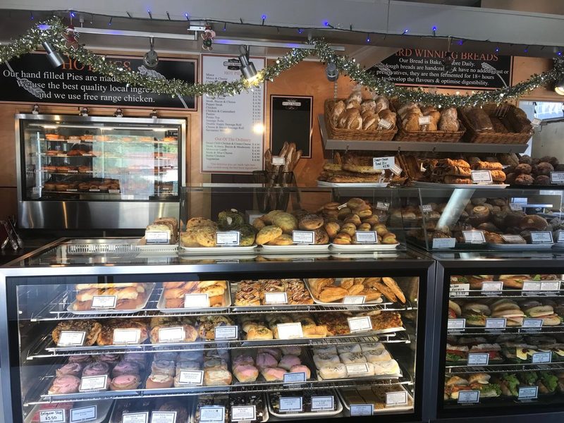 Interior counter filled with breads, pastries, doughnuts and sandwiches beneath the bakery's display signs.