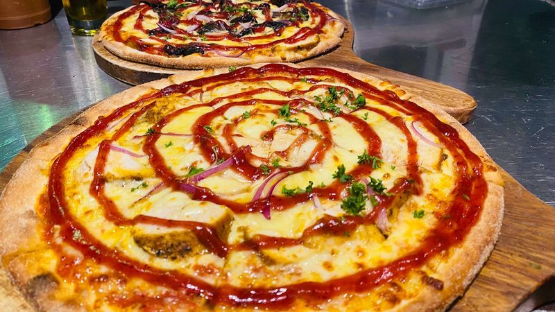 Two finished wood-fired pizzas on wooden serving boards in Scoozi's kitchen.