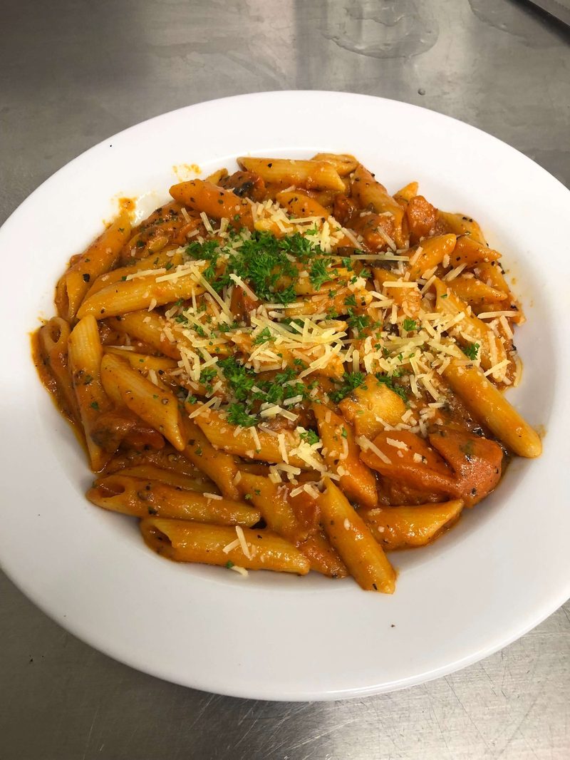 A bowl of penne pasta in tomato sauce, topped with grated cheese and parsley.