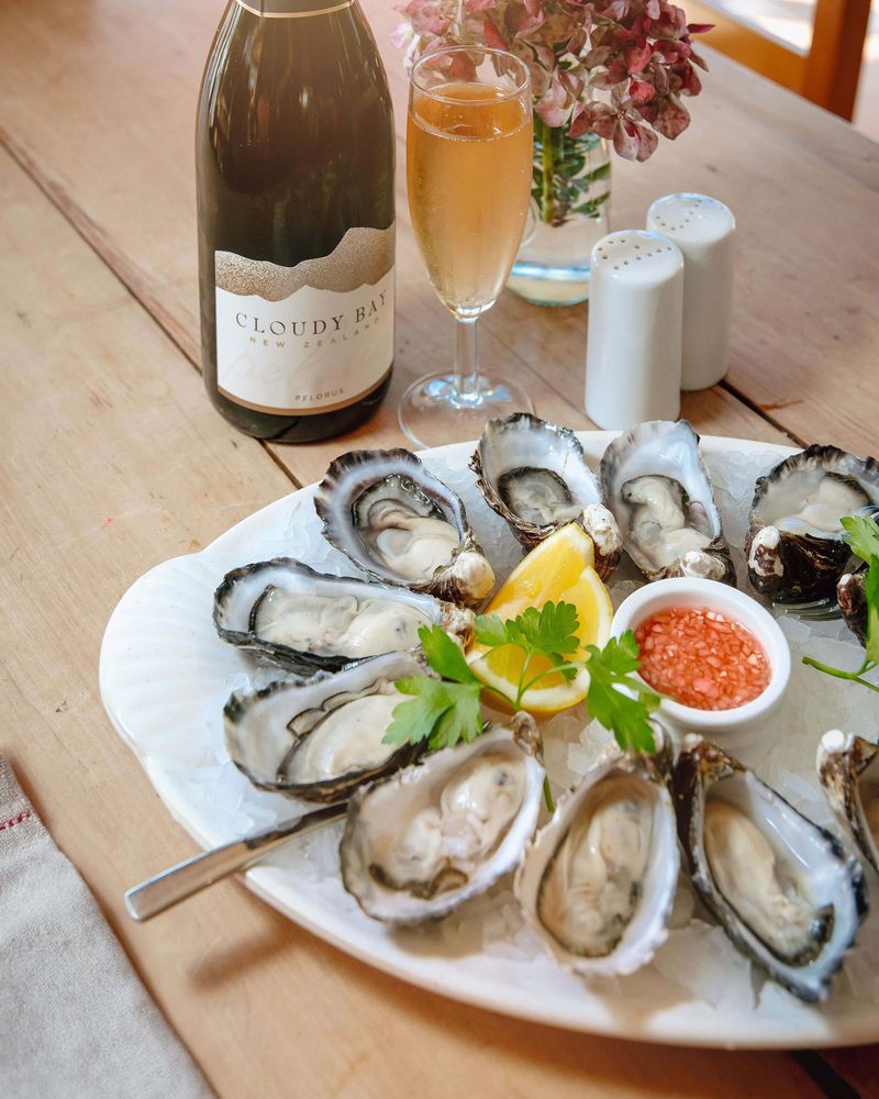 Fresh oysters on ice with lemon, shallot dressing, and a bottle and glass of Cloudy Bay Pelorus.