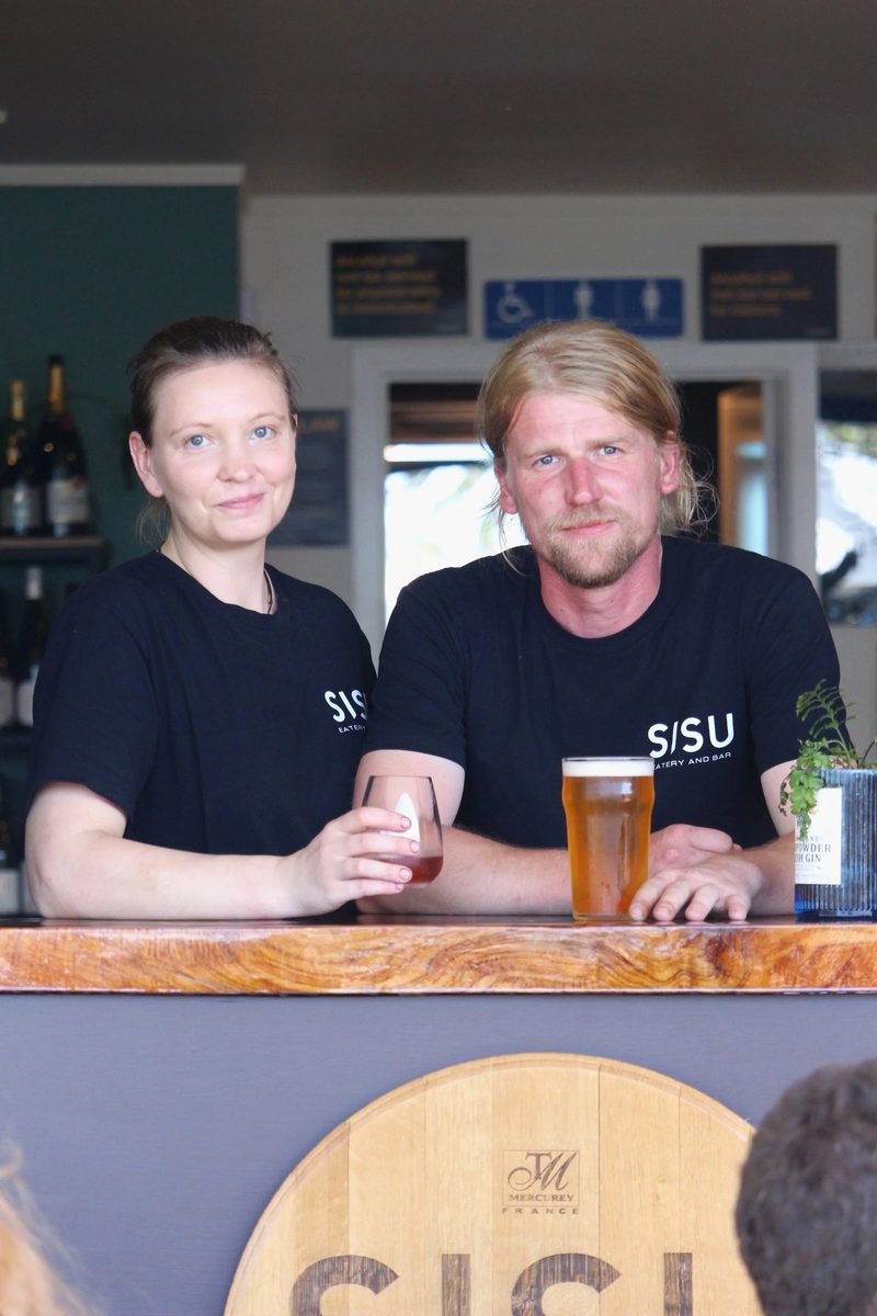 Sisu's two owners behind the venue's timber bar in branded shirts, with drinks and bottle shelves visible.
