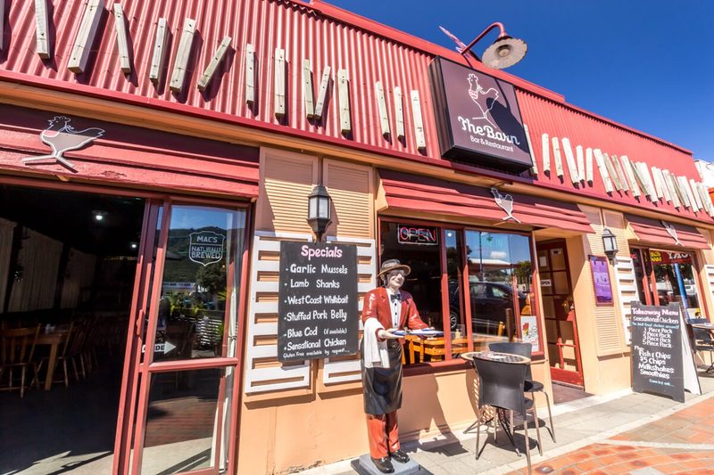 Street-facing red shopfront with The Barn signage, entrance, menu boards and outdoor table.