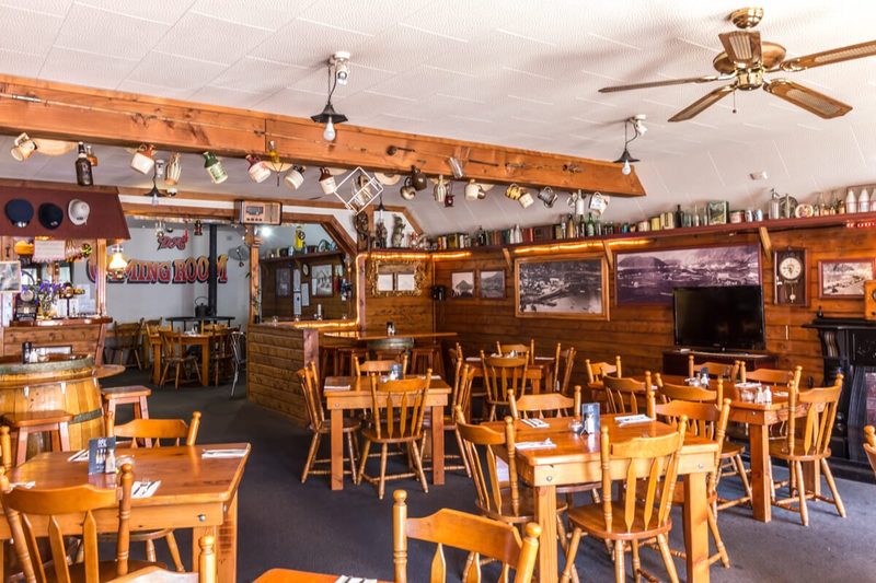 Wood-lined main dining room with set tables, barrel decor, historic photographs and bar area.