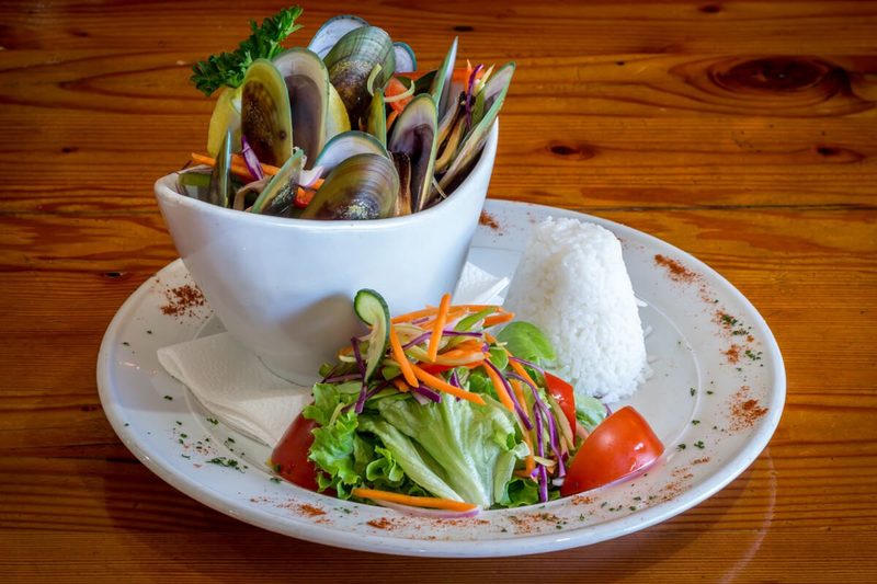 Green-lipped mussels served with rice and a fresh salad on a wooden table.