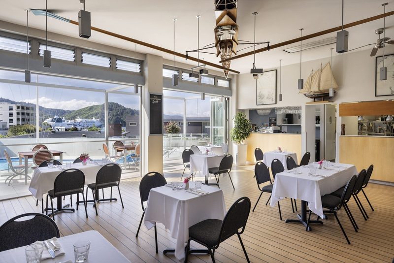 Bright nautical-themed Chartroom dining room with set tables, open kitchen and harbour outlook.