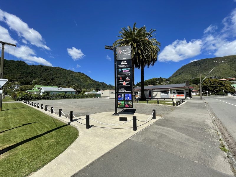 Daytime view of The Crow Tavern, its roadside sign, car park, palm trees and surrounding hills.