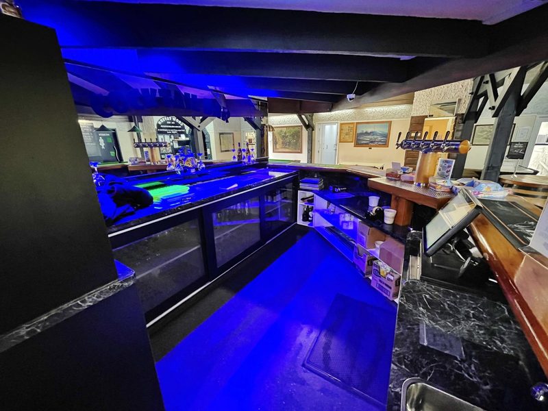 View behind the blue-lit bar counter with beer taps, pool table and historic pictures on the walls.