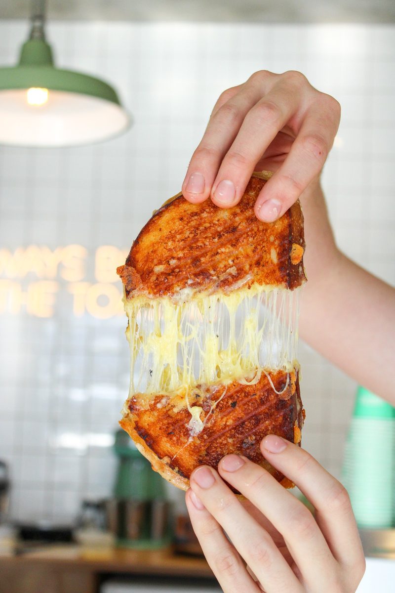 A toasted sandwich being pulled apart to show long strands of melted cheese inside.
