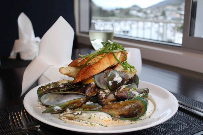 Green-lip mussels in a creamy sauce with toasted bread, photographed by a harbour-facing window.