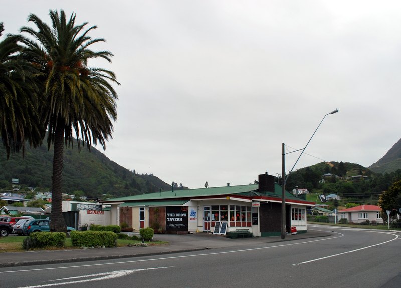 Low green-roofed tavern building beside a road and a large palm tree, Picton